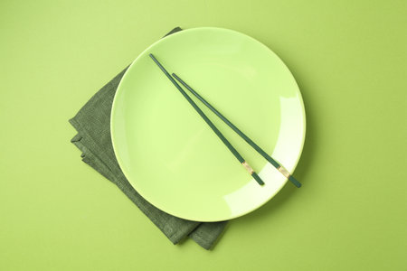 Stylish plate, chopsticks and napkin on green background, top viewの写真素材