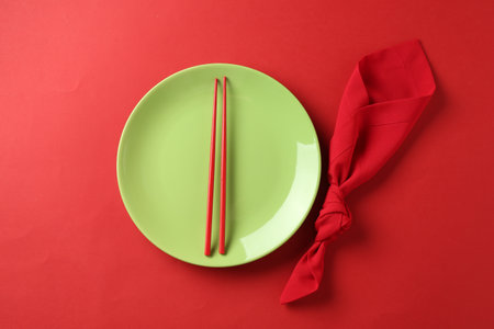 Stylish plate, chopsticks and napkin on red background, flat layの写真素材