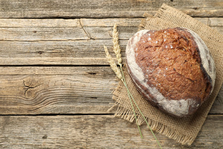 Loaf of fresh bread and spikes on wooden table, flat lay. Space for text