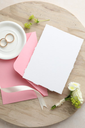 Wedding invitation card, envelope, golden rings, ribbon and floral decor on color textured table, top viewの写真素材