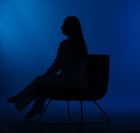 Silhouette of woman on chair against dark blue backgroundの写真素材