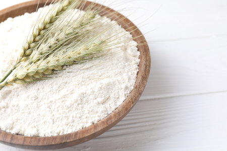 Flour and green wheat spikes in bowl on white wooden table, closeup. Space for textの写真素材