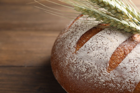 Fresh bread and green wheat spikes on wooden table, closeup. Space for textの写真素材