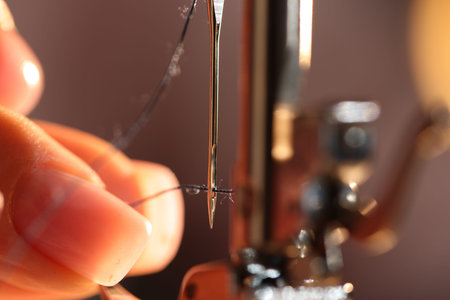Woman threading sewing machine needle on blurred grey background, macro view