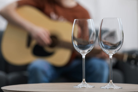Empty wineglasses on table and man playing guitar indoors, selective focusの写真素材
