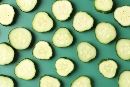 Slices of fresh cucumbers on green background, flat layの写真素材