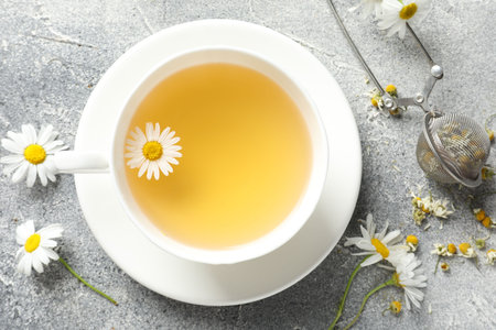 Tasty chamomile tea, infuser and flowers on light grey table, flat layの写真素材
