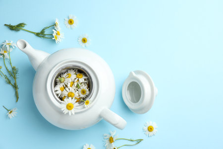 Teapot with chamomile flowers on light blue background, flat lay. Space for textの写真素材