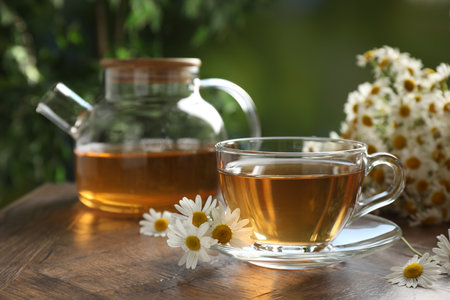 Aromatic tea in glass cup and chamomile flowers on wooden table, closeupの写真素材