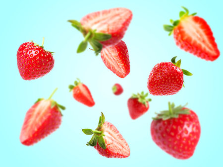 Yummy fresh strawberries swirling in air against light blue backgroundの写真素材