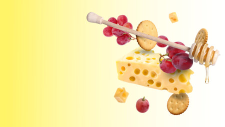 Cheese, grapes, crackers and honey in air on yellow gradient background. Tasty appetizers for cheese boardの写真素材