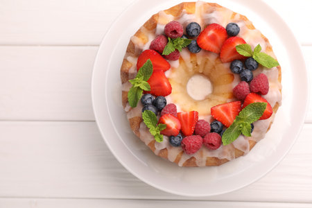 Delicious bundt cake with berries, glaze and mint on white wooden table, top view. Space for textの写真素材