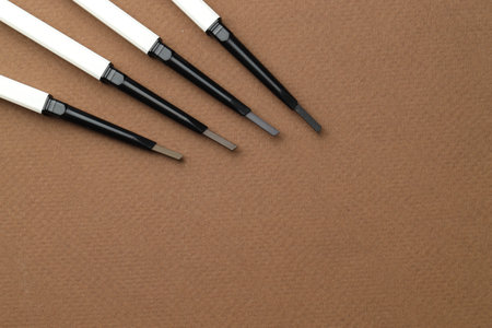 Different eyebrow pencils on brown background, flat lay. Space for textの写真素材