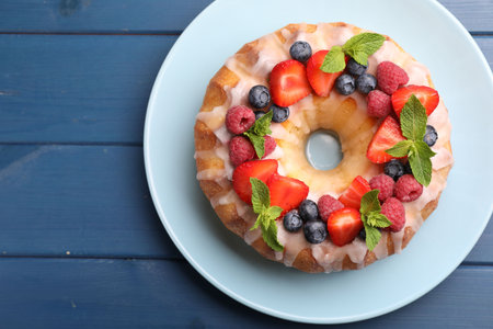 Delicious bundt cake with berries, glaze and mint on blue wooden table, top view. Space for textの写真素材