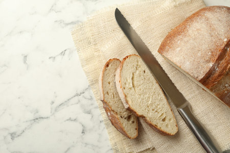 Pieces of fresh bread and knife on white marble table, flat lay. Space for text