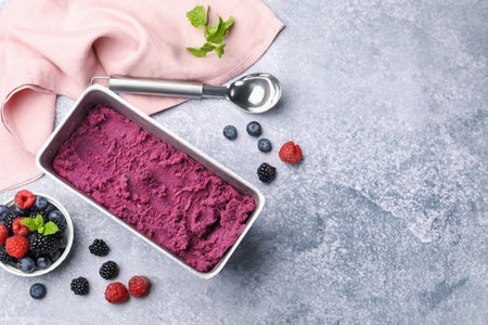 Delicious sorbet in metal container, fresh berries and spoon on gray table, flat lay. Space for textの写真素材