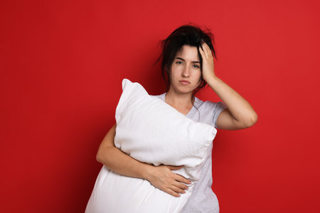 Woman with pillow suffering from hangover on red backgroundの写真素材