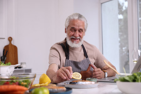 Elderly man putting slice of lemon onto salmon fish at white table indoorsの写真素材