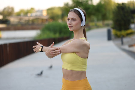 Young sportswoman in headphones doing morning exercise outdoors