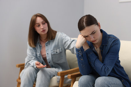 Woman apologizing to her offended friend on armchair near gray wall at home, selective focusの写真素材
