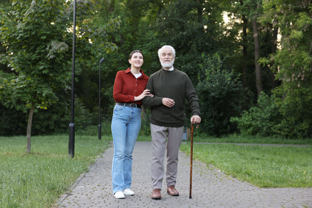 Smiling caregiver supporting elderly man who using walking cane outdoorsの写真素材