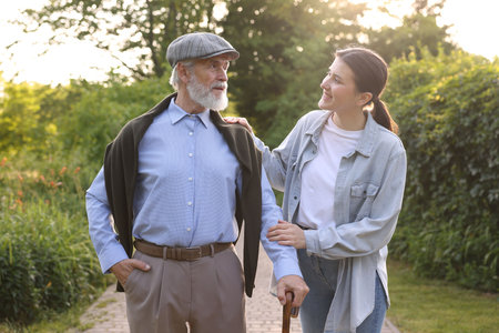 Smiling caregiver supporting elderly man with walking cane outdoorsの写真素材