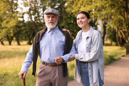 Smiling caregiver supporting elderly man with walking cane outdoorsの写真素材