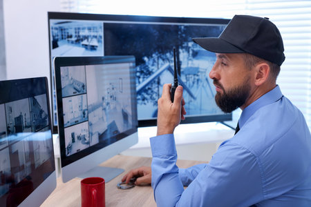 Security guard monitoring CCTV cameras and using walkie talkie in office