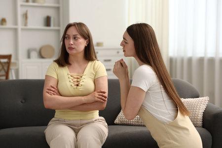 Woman apologizing to her offended friend on sofa at homeの写真素材