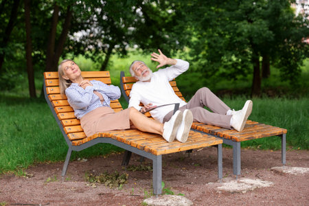 Lovely senior couple resting on wooden sunbeds in parkの写真素材