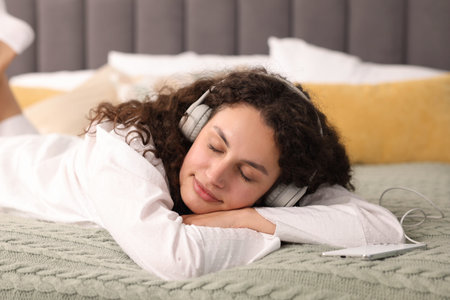 Young woman with headphones listening to music on bed at home