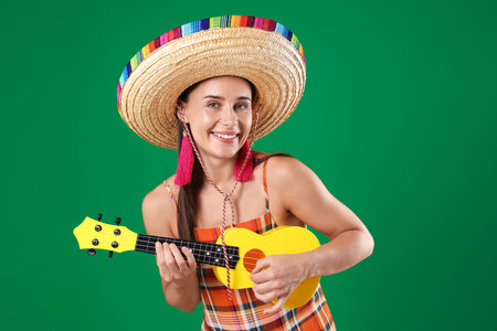 Smiling woman in sombrero hat playing ukulele on green background