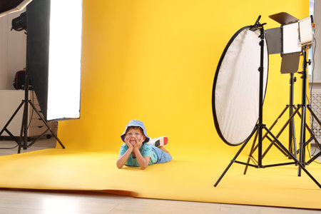 Little boy on yellow background in photo studio with professional equipmentの写真素材