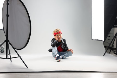 Little boy on light gray background in photo studio with professional equipmentの写真素材