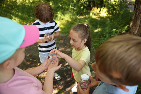 Children in nature. Cute little girl putting snail into jar outdoors