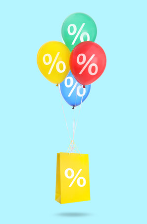 Shopping bag and balloons with percent signs in air against light blue backgroundの写真素材
