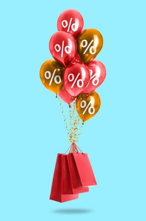 Balloons with percent signs tied to shopping bags in air against light blue backgroundの写真素材