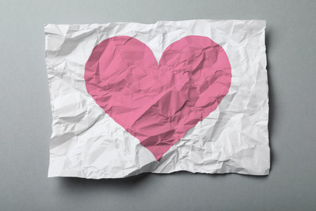 Crumpled sheet of paper with pink heart on grey background, top viewの写真素材