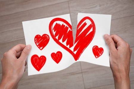 Betrayal. Man tearing sheet of paper with red hearts indoors, closeupの写真素材