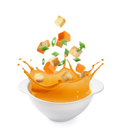 Croutons and pumpkin cubes falling into bowl of soup against white backgroundの写真素材