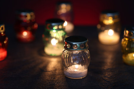 Many grave candles on black table against red background, closeup