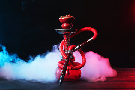 Hookah on wooden table with smoke in color lights against black backgroundのeditorial素材