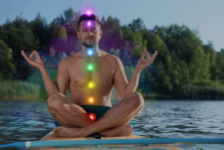 Man meditating in Lotus pose on SUP board. Rainbow lights representing chakras. Aura around him
