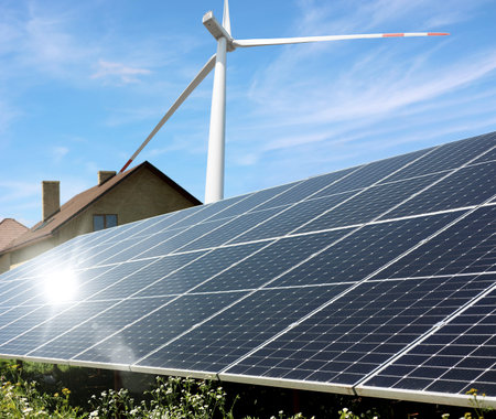 Solar panels and wind turbine near house outdoors. Alternative energy source