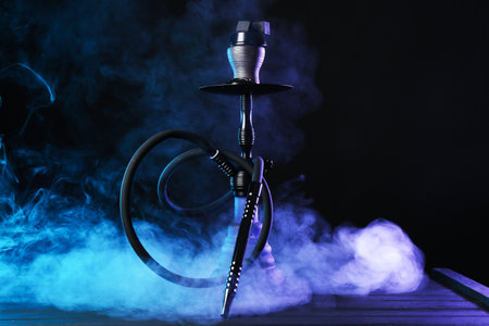 Hookah on wooden table with smoke in color lights against black backgroundのeditorial素材