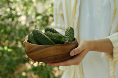 Woman with bowl of fresh cucumbers against blurred green background, closeupのeditorial素材