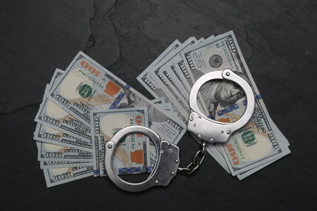 Corruption. Handcuffs and dollar bills on black table, flat lay