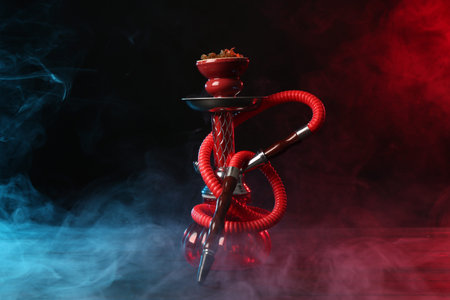 Hookah on wooden table with smoke in color lights against black background