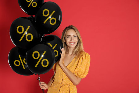 Happy woman holding balloons with percent signs against red background.