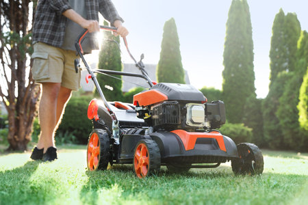 Man cutting green grass with lawn mower in garden, closeup